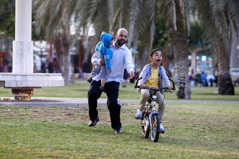Mahmoud Al Haji teaches his son Ibrahim, 7, to ride his bike while holding his younger son Khalid, 2, at the Khalidiyah public garden in Abu Dhabi. Christopher Pike / The National
