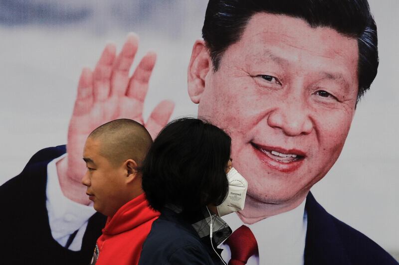 Pedestrians, one wearing a mask, walk by a poster of Chinese President Xi Jinping on a street in Beijing, Thursday, Oct. 26, 2017. China's ruling Communist Party has praised President Xi as a Marxist thinker, adding to intense propaganda promoting Xi's personal image as he begins a second five-year term as leader. (AP Photo/Andy Wong)