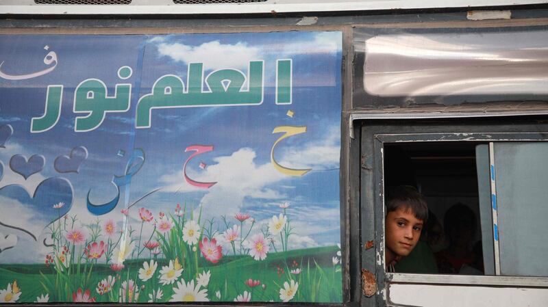 A displaced Syrian child peeks out of a window of bus that was converted into a classroom.
