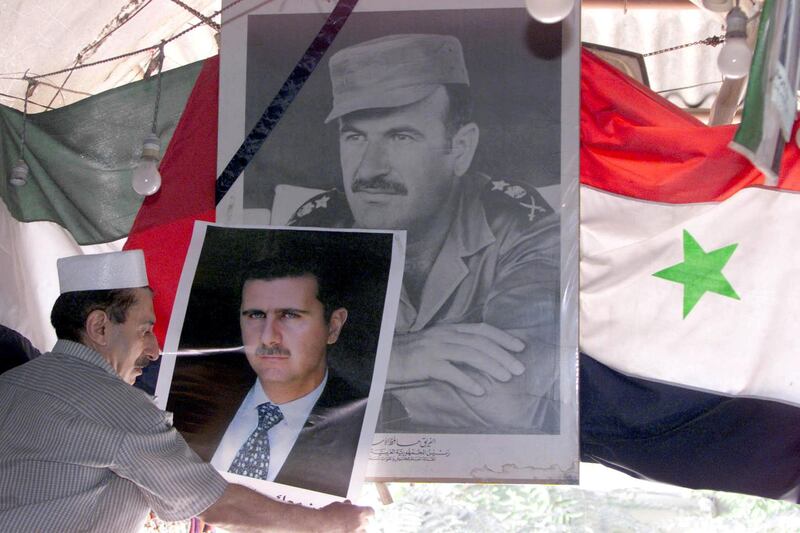 (FILES) In this file photo taken on June 20, 2000, a Syrian merchant places a picture of heir apparent Bashar al-Assad next to a portrait of his father, Syria's late President Hafez al-Assad, in front of a national flag outside his shop in the capital Damascus. - President Bashar al-Assad, whose family has ruled Syria for over half a century, faces an election this week meant to cement his image as the only hope for recovery in the war-battered country, analysts say. (Photo by RAMZI HAIDAR / AFP)
