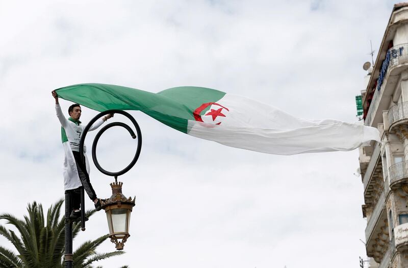 FILE PHOTO: A demonstrator stands on a street pole as he carries a national flag during a protest to push for the removal of the current political structure, in Algiers, Algeria April 5, 2019. REUTERS/Ramzi Boudina/File Photo