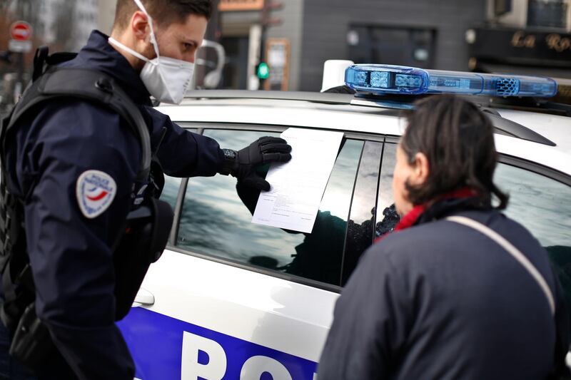 A police officer issues a fine to a woman who is outdoors without permission, at the entrance of the open-air market of Belleville, in Paris on March 20, 2020. AP Photo