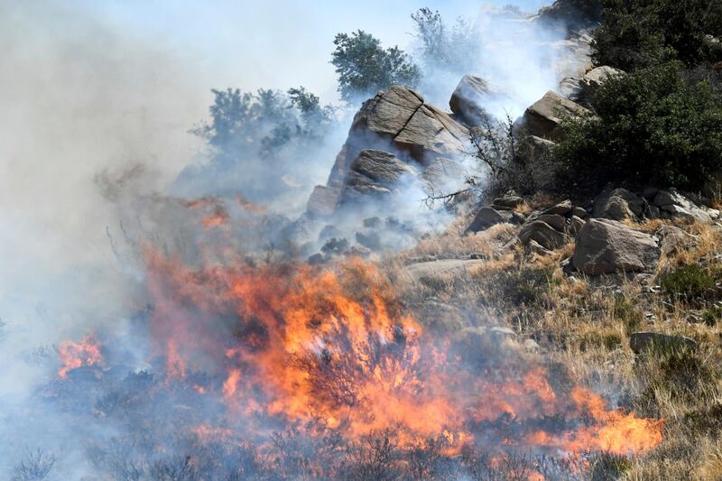 Flames from a brush fire flare around the rocks in San Bernardino, California. James Quigg / The Daily Press via AP