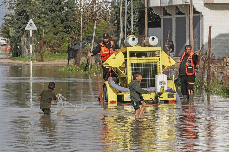 Members of Palestinian Civil Defence work on a flooded street as boys cross in Rafah in the southern Gaza Strip.   AFP