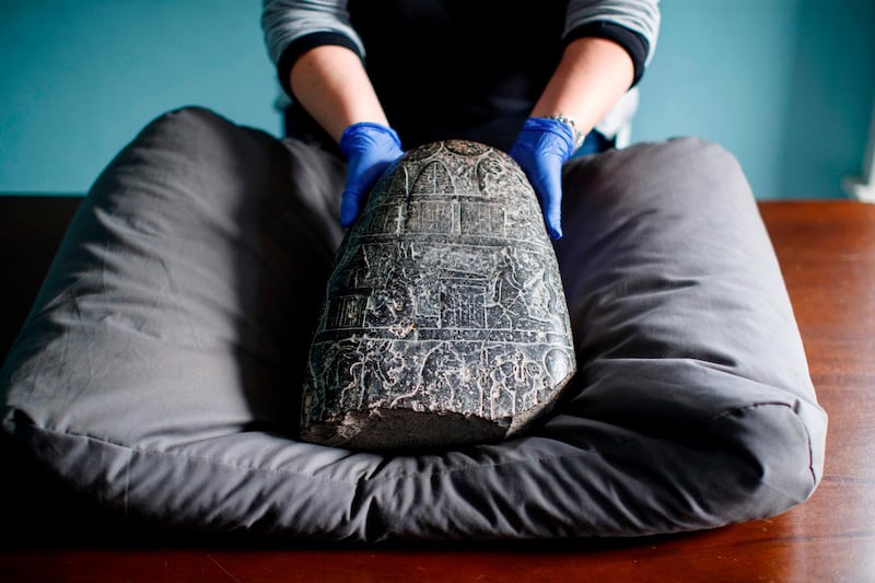 TOPSHOT - A gallery assistant poses with a Babylonian cuneiform kudurru (boundary stone) which was looted from Iraq on March 19, 2019 at the British museum in London. The kudurru which was seized at London's Heathrow airport in 2012 was handed over to representatives of the Iraq embassy today at the British museum. / AFP / Tolga Akmen
