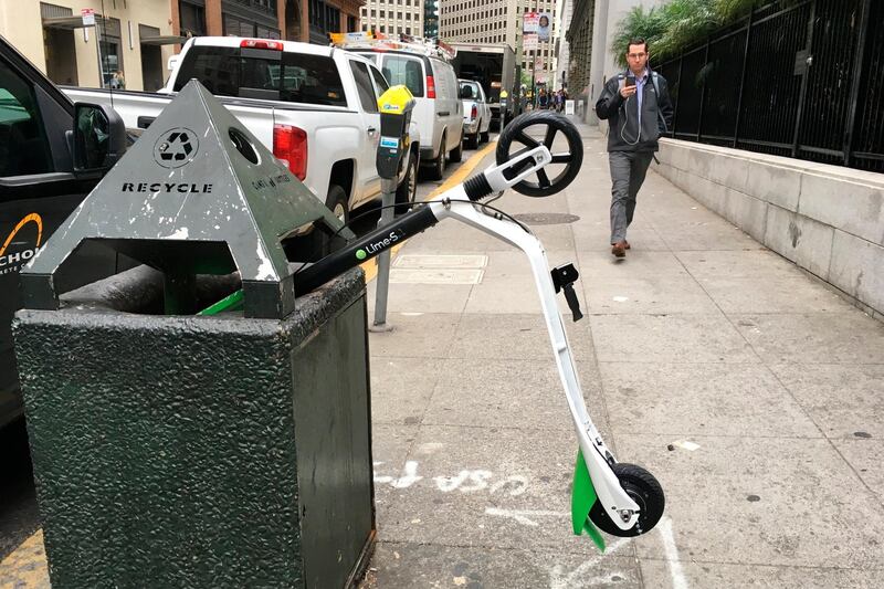 In this photo taken May 14, 2018, a man walks past an electric scooter that was dumped into a trash can in San Francisco. Tired of San Francisco streets being used as a testing ground for the latest delivery technology and transportation apps, city leaders are considering requiring businesses to get permits before trying out new high-tech ideas in public. Supporters of the legislation, which the Board of Supervisors will take up Tuesday, Dec. 10, 2019, say it would be the first of its kind in the U.S. They say it's long overdue in a city that's a hub for major tech companies but is more accustomed to reacting to the sudden arrival of new technology, such as when hundreds of dockless electric scooters appeared overnight last year. (AP Photo/Janie Har)