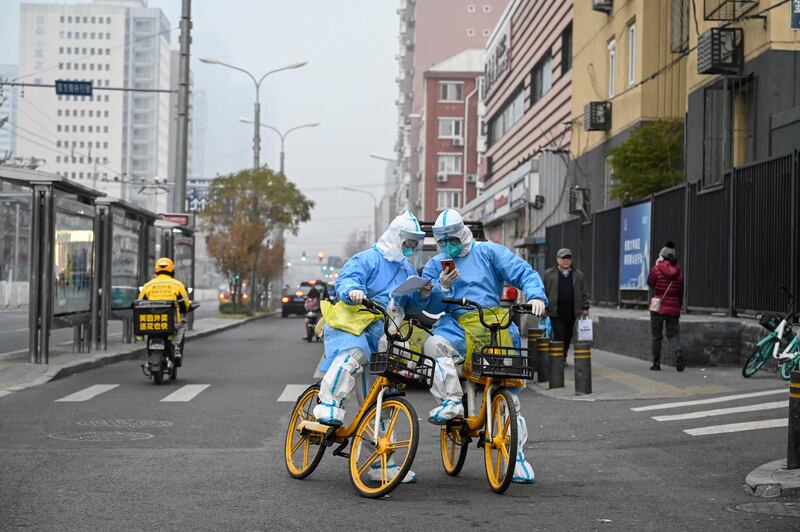 Health workers in personal protective equipment carrying Covid-19 coronavirus testing swabs and tubes on bicycles in Beijing. AFP