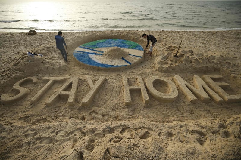 Palestinian artists work on a sand sculpture depicting the earth with a message reading "Stay Home" along a beach in Gaza City. AFP