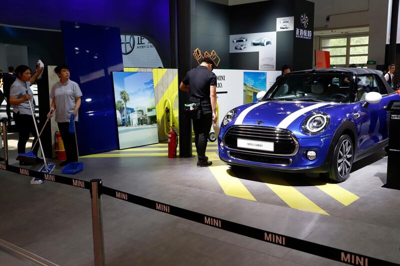 In this April 26, 2018, photo, cleaners wait near a MINI Cooper Cabrio displayed at the China Auto Show in Beijing. BMW Group and China's biggest SUV brand, Great Wall Motor, announced Tuesday, July 10, 2018, a partnership to produce electric MINI vehicles in China. (AP Photo/Ng Han Guan)