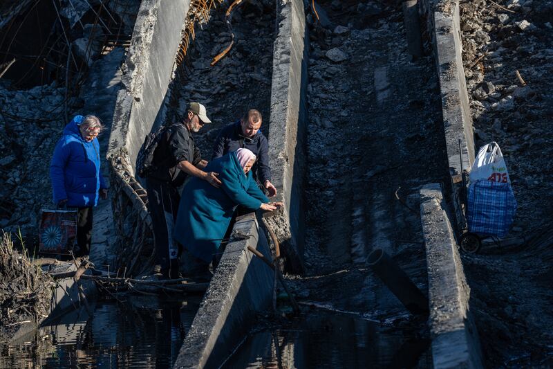 An elderly woman is helped across a damaged bridge in Bakhmut in October 2022. Getty Images