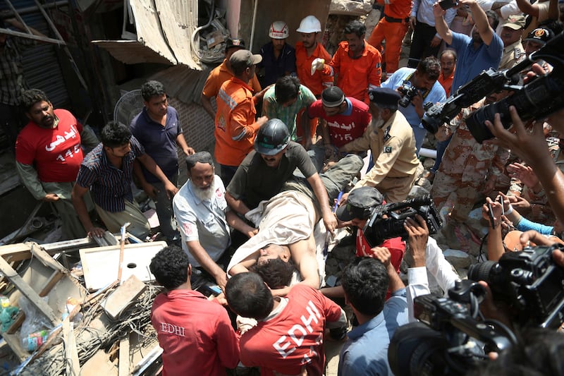 Pakistani volunteers carry an injured person rescued from a collapsed residential building in Karachi on July 18, 2017. Shakil Adil / AP