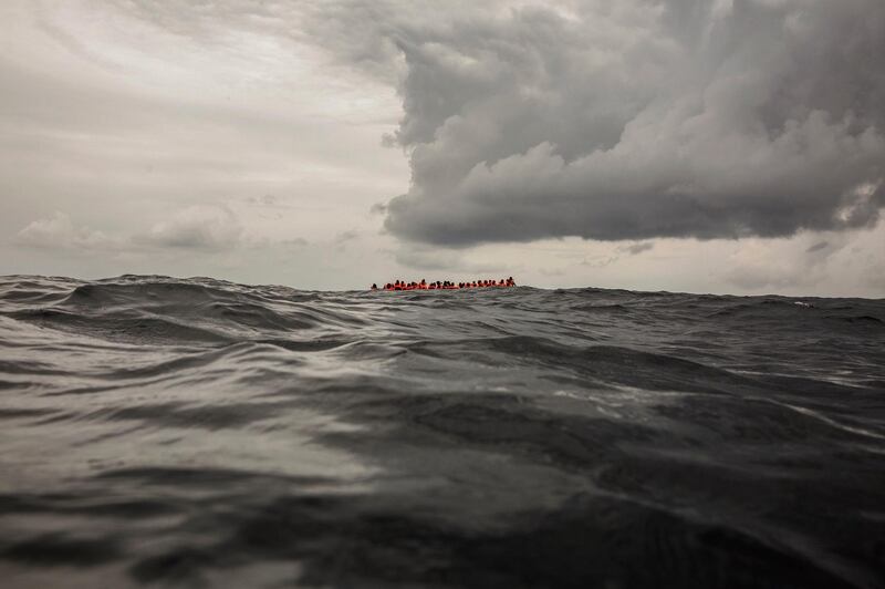 FILE - In this Sunday Feb. 18, 2018 file photo, refugees and migrants wait to be rescued by aid workers 60 miles north of Al-Khums, Libya. A migration official says survivors have told rescuers that up to 117 migrants might have died when a rubber dinghy capsized in the Mediterranean Sea off Libya. Flavio Di Giacomo of International Organization for Migration says three survivors were plucked to safety by an Italian navy helicopter Friday, Jan. 18, 2019 and they say 120 were aboard when the dinghy left Libya. The Italian Coast Guard says Libya asked a nearby cargo ship to search for survivors but reported that no one was found. (AP Photo/Olmo Calvo, File )