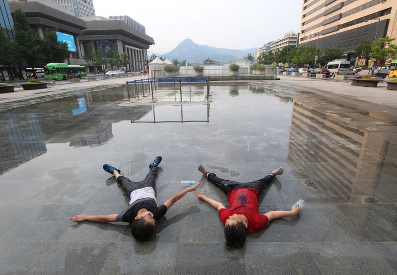 Boys lie in wait for a fountain to sprinkle water on them in Seoul, South Korea. Ahn Young-joon / AP Photo
