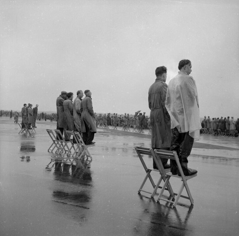 Enthusiasts stand on chairs in the rain to get a better view of the aircraft as they fly past at the Farnborough Airshow 1956.