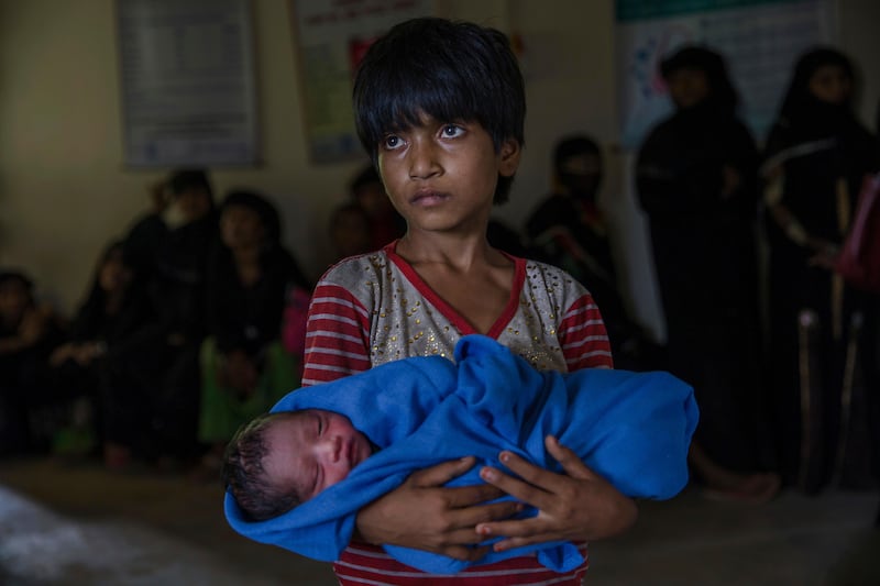 Rohingya Muslim girl Afeefa Bebi, who recently crossed over from Myanmar into Bangladesh, holds her few-hours-old brother as doctors check her mother Yasmeen Ara at a community hospital in Kutupalong refugee camp, Bangladesh, Wednesday, Sept. 13, 2017. The family crossed into Bangladesh on Sept. 3. Recent violence in Myanmar has driven hundreds of thousands of Rohingya Muslims to seek refuge across the border in Bangladesh. But Rohingya have been fleeing persecution in Buddhist-majority Myanmar for decades, and many who have made it to safety in other countries still face a precarious existence. (AP Photo/Dar Yasin)