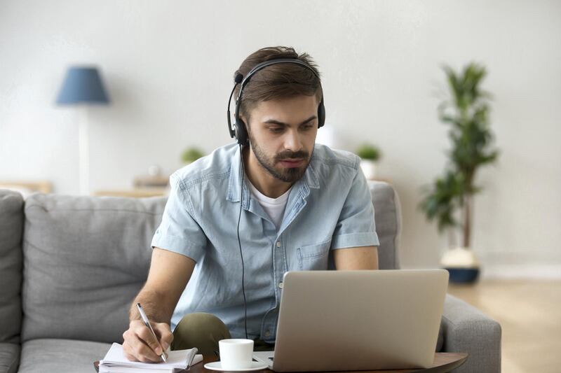 Serious young man looking at laptop wearing headset learning foreign language, training knowledge listening webinar making notes, online study, e-coaching, distance education, e-learning concept