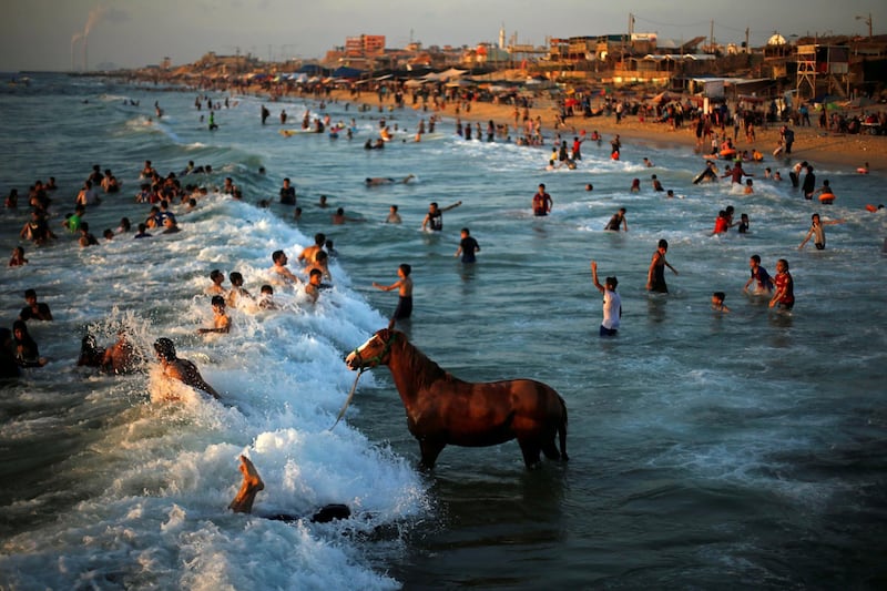 A Palestinian man washes his horse in the waters of the Mediterranean Sea as people swim on a hot day in the northern Gaza Strip June 18, 2019. REUTERS/Mohammed Salem     TPX IMAGES OF THE DAY