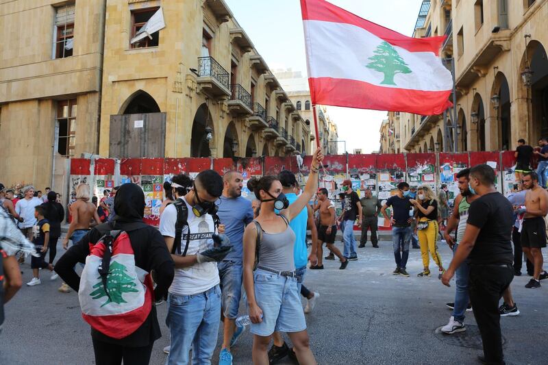 epa08595570 Protesters wave a Lebanese flag during protests near the parliament in Beirut, Lebanon, 10 August 2020. According to reports, anti-government protests continued in Lebanon despite the resignation of three ministers and several members of the parliament, as protesters are demanding the resignation of the government and all those responsible for the port explosion be held accountable. Beirut governor said at least 200 people were killed in the explosion on 04 August and dozens are still missing.  EPA/NABIL MOUNZER