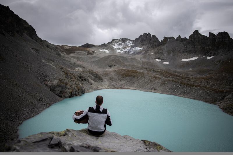 A hiker plays his accordion with view of Wildlake and the Pizol glacier on the sideline of a commemoration for the 'dying' glacier of Pizol mountain, pictured in the background, in Wangs, Switzerland. AP