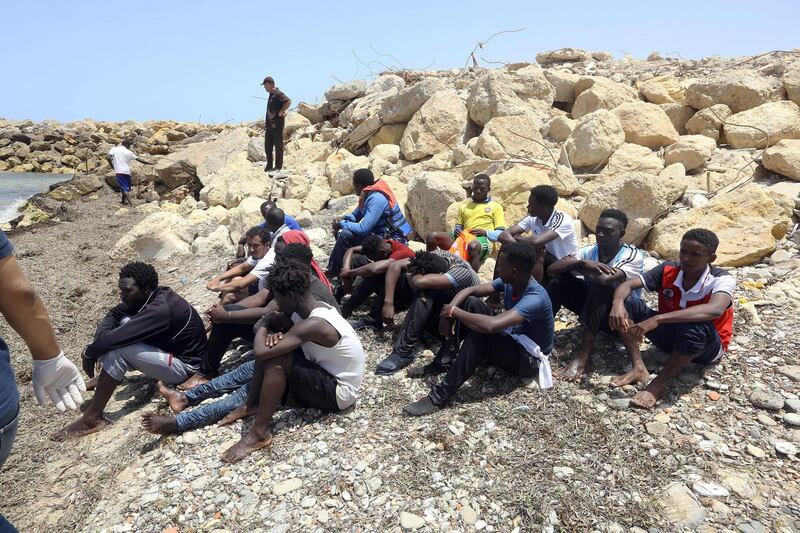 TOPSHOT - Migrants who survived the sinking of an inflatable dinghy boat off of the coast of Libya are grouped on the shore of al-Hmidiya, east of the capital Tripoli on June 29, 2018.  The bodies of three babies were recovered and around 100 people were missing after a migrant boat sank off the coast of Libya, survivors and the coastguard said. / AFP / Mahmud TURKIA
