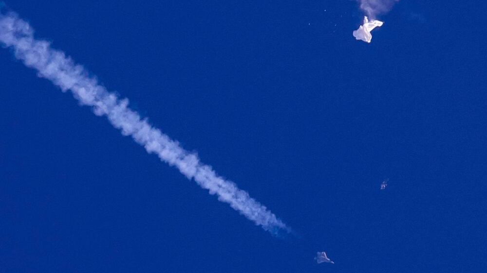 In this photo provided by Chad Fish, the remnants of a large balloon drift above the Atlantic Ocean, just off the coast of South Carolina, with a fighter jet and its contrail seen below it, Saturday, Feb.  4, 2023.  The downing of the suspected Chinese spy balloon by a missile from an F-22 fighter jet created a spectacle over one of the state’s tourism hubs and drew crowds reacting with a mixture of bewildered gazing, distress and cheering.  (Chad Fish via AP)