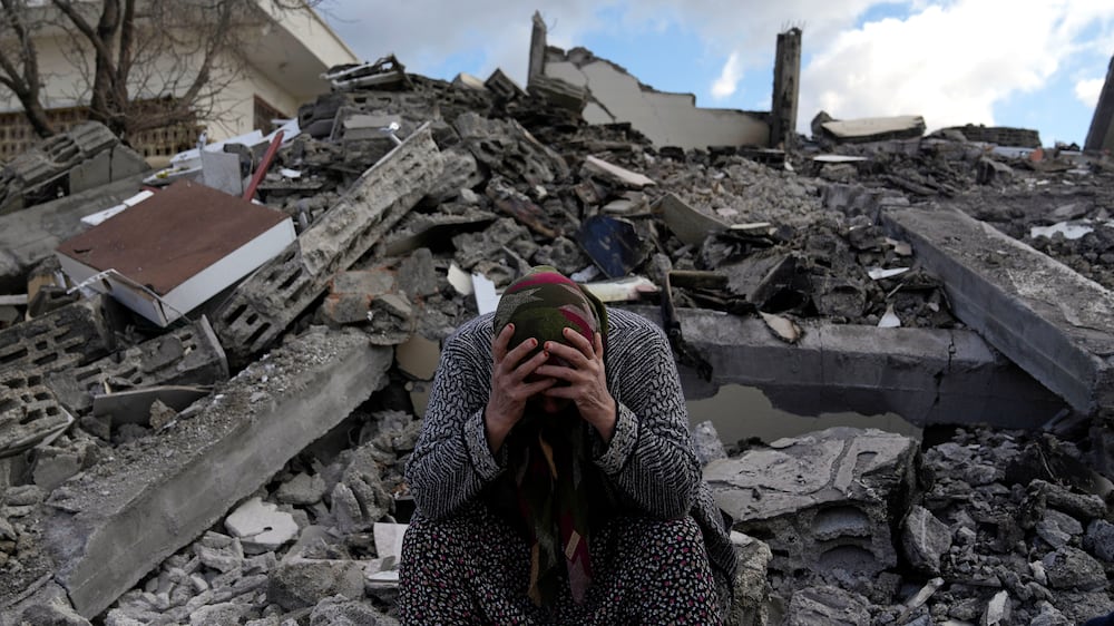 A woman sits on the rubble as emergency rescue teams search for people under the remains of destroyed buildings in Nurdagi town on the outskirts of Osmaniye city southern Turkey, Tuesday, Feb.  7, 2023.  A powerful earthquake hit southeast Turkey and Syria early Monday, toppling hundreds of buildings and killing and injuring thousands of people.  (AP Photo / Khalil Hamra)