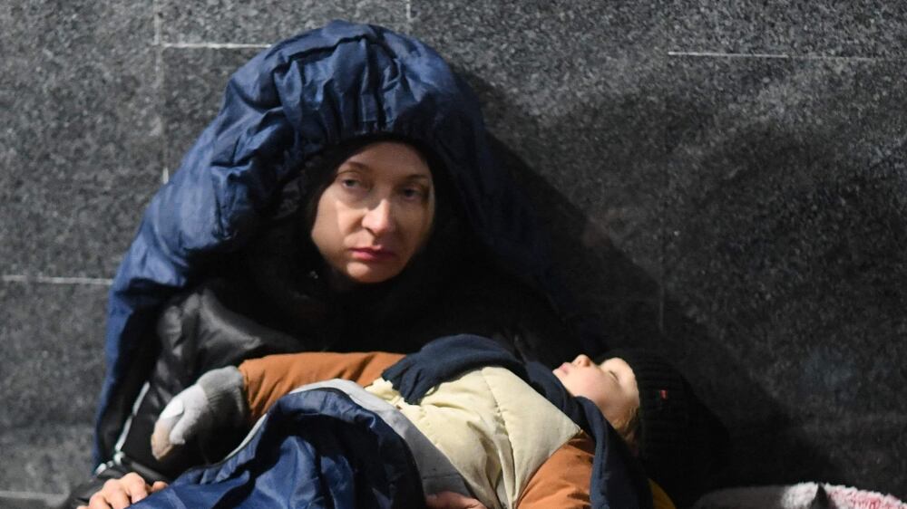 A woman holds her sleeping child while sitting on the ground at Lviv central train station in Western Ukraine on February 26, 2022.  - Moscow ordered its troops to advance in Ukraine "from all directions" on Saturday, as the Ukrainian capital Kyiv imposed a blanket curfew after fighting in the city that saw Russian troops pushed back.  (Photo by Daniel LEAL  /  AFP)