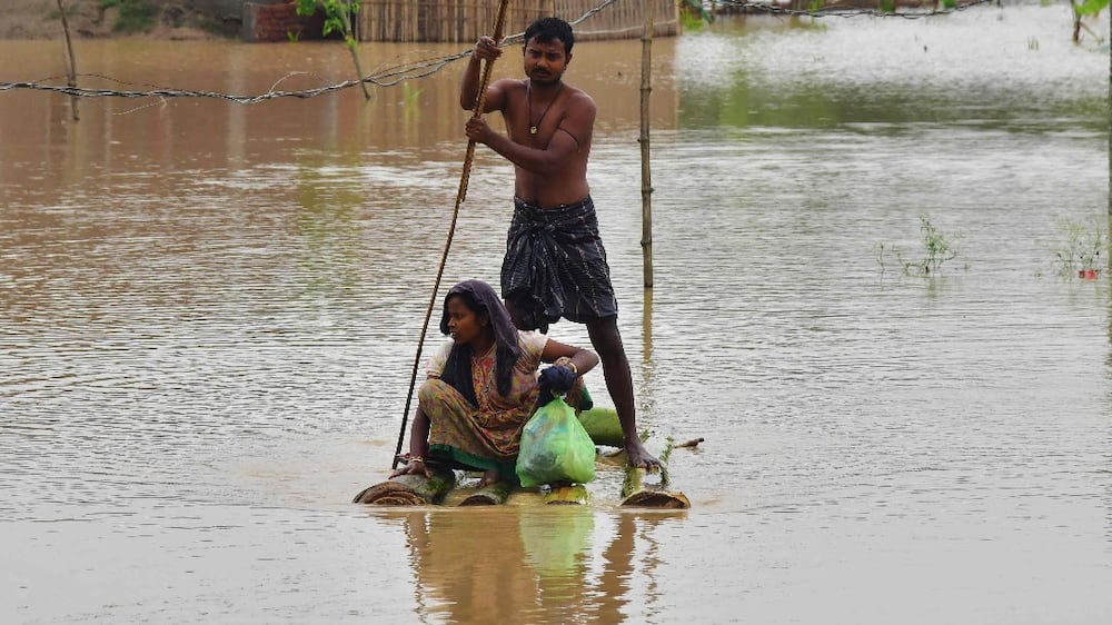 Villagers make their way on a raft past homes in a flooded area after heavy rains in Nagaon district, Assam state, on May 21, 2022.  - Heavy rains have caused widespread flooding in parts of Bangladesh and India, leaving millions stranded and at least 57 dead, officials said on May 21.  (Photo by Biju BORO  /  AFP)