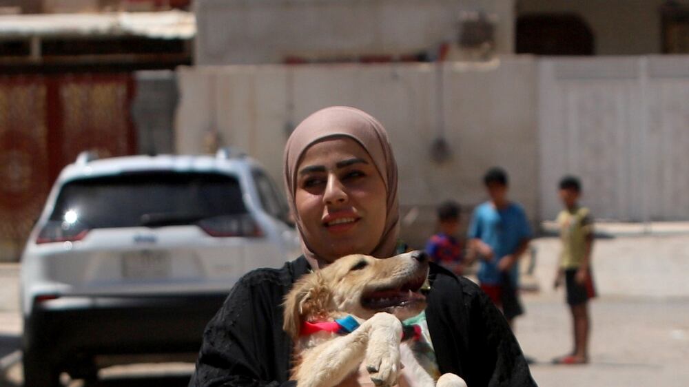 Zainab Al-Obeidy, who set up a shelter for stray dogs at her home, carries a dog on the street in Amarah, Iraq July 9, 2021. Picture taken July 9, 2021. REUTERS/Essam al-Sudani