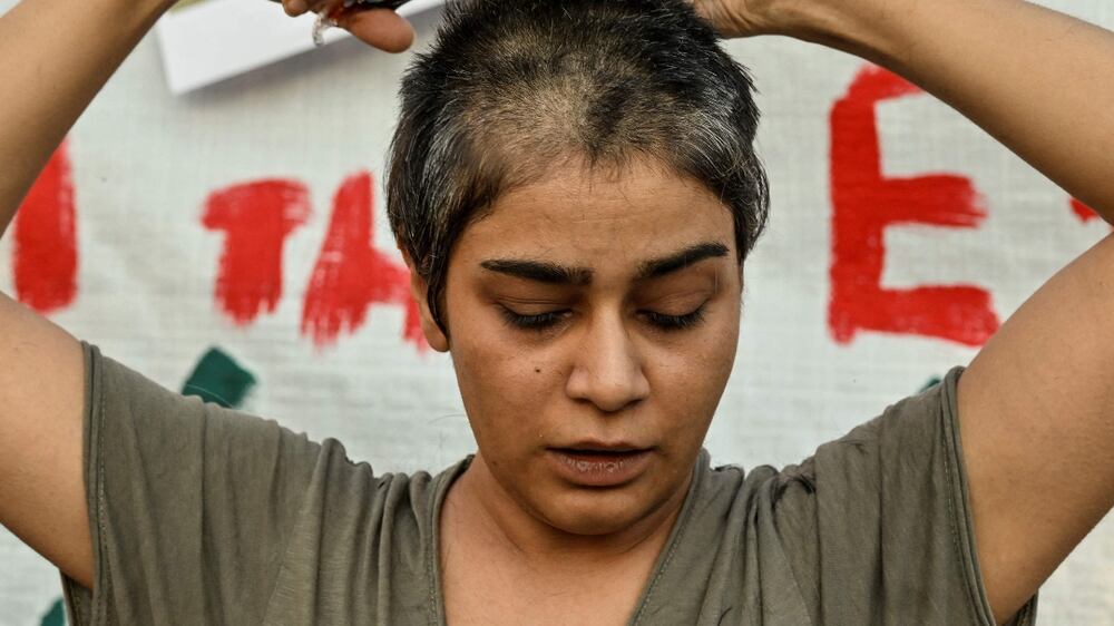 Eli, an Iranian refugee woman living in Greece cuts her hair during a demonstration by Iranians living in Greece in central Athens on September 24, 2022, following the death of an Iranian woman after her arrest by the country's morality police in Tehran.  - Mahsa Amini, 22, was on a visit with her family to the Iranian capital Tehran, when she was detained on September 13, 2022, by the police unit responsible for enforcing Iran's strict dress code for women, including the wearing of the headscarf in public.  (Photo by Louisa GOULIAMAKI  /  AFP)