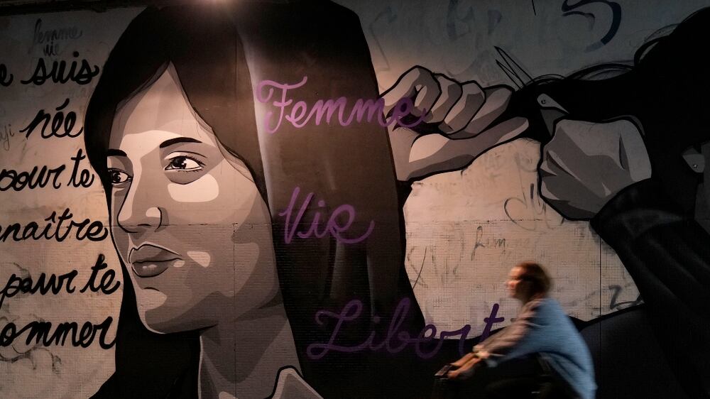 A woman rides bicycle front of a mural signed by Clacks-one and Heartcraft_Street art, depicting women cutting their hair to show support for Iranian protesters standing up to their leadership over the death of a young woman in police custody, in a tunnel in Paris, France, Wednesday, Oct.  5, 2022.  Thousands of Iranians have taken to the streets over the last two weeks to protest the death of Mahsa Amini, a 22-year-old woman who had been detained by Iran's morality police in the capital of Tehran for allegedly not adhering to Iran's strict Islamic dress code.  Mural reads : "I was born to know you to name you", "Woman Life Freedom". (AP Photo / Francois Mori)