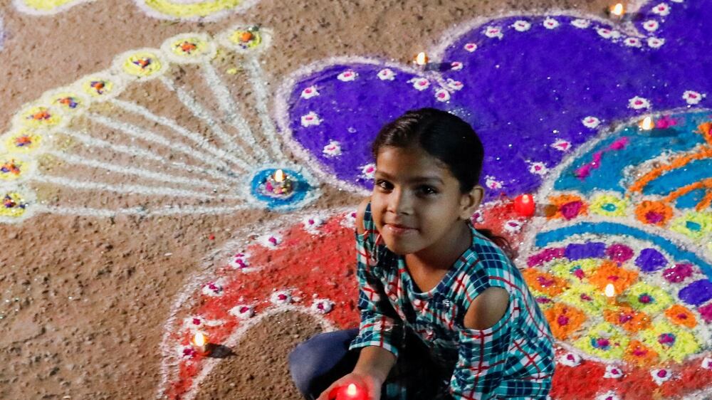A girl poses with a rangoli, mural made out of coloured powders, outside her home during Diwali, the Hindu festival of lights, in Karachi, Pakistan, October 24, 2022.  REUTERS / Akhtar Soomro