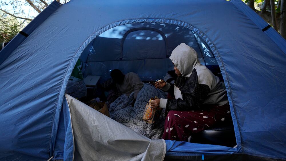 Grace Enjei, 24, right, and Daniel Ejuba, 20, migrants from Cameroon, sit in a blue tent behind the House of Cooperation located inside a United Nations-controlled buffer zone cutting across Nicosia, the capital of ethnically divided Cyprus on Wednesday, Dec.  1, 2021.  The Cameroonian asylum seekers crossed from the island's breakaway Turkish Cypriot north about six months ago and got stuck in the buffer zone amid a Cypriot government crackdown on migrants crossing the porous buffer zone.  (AP Photo / Petros Karadjias)