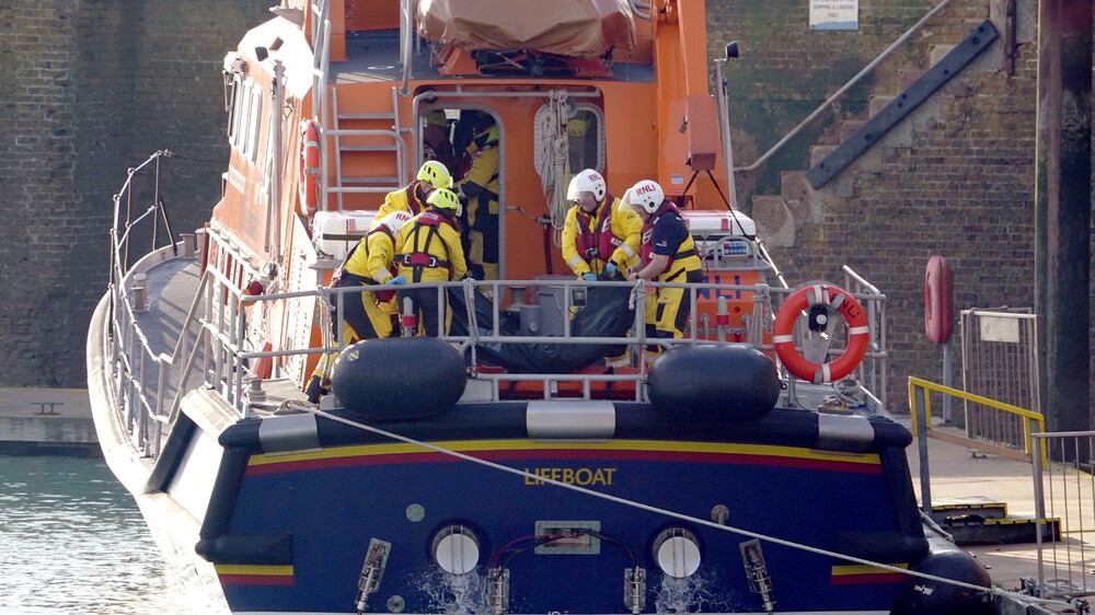 Members of the Dover lifeboat place a body bag on a stretcher after returning to the Port of Dover after a large search and rescue operation launched in the Channel off the coast of Dungeness, in Kent, Wednesday Dec.  14, 2022, following an incident involving a small boat likely to have been carrying migrants.  Helicopters and lifeboats have been dispatched to the English Channel off the coast of Kent in southern England to rescue a small boat in distress, authorities said Wednesday.  (Gareth Fuller / PA via AP)