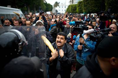 A Tunisian protester holding a baguette talks to riot policemen during a demonstration in Tunis on January 18, 2011. Riot police fired tear gas and clashed with protesters on January 18 at a small protest rally against Tunisia's new government in the centre of the capital, AFP reporters on the ground saw. Around 100 protesters chanted slogans against the RCD party of ousted president Zine El Abidine Ben Ali. "We can live on bread and water alone but not with the RCD," they said. Riot police dispersed the rally -- one of several expected on Tuesday.  AFP PHOTO / MARTIN BUREAU