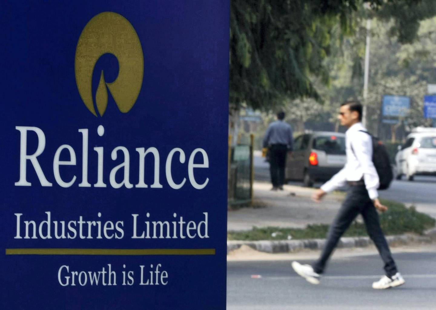 A man walks past a Reliance Industries Limited sign board installed on a road divider in the western Indian city of Gandhinagar January 17, 2014. Indian energy conglomerate Reliance Industries reported a nearly flat profit of 55.11 billion rupees ($895 million) for the December quarter but beat analyst estimates, helped by stable margins in its main refining business. REUTERS/Amit Dave (INDIA - Tags: BUSINESS ENERGY) - GM1EA1H1L8B01