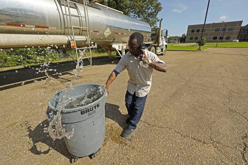 Santonia Matthews, a custodian at Forest Hill High School in Jackson, Miss. , hauls away a trash can filled with water from a tanker in the school's parking lot, Wednesday, Aug.  31, 2022.  The tanker is one of two placed strategically in the city to provide residents non-potable water.  The recent flood worsened Jackson's longstanding water system problems and the state Health Department has had Mississippi's capital city under a boil-water notice since late July.  (AP Photo/Rogelio V.  Solis)