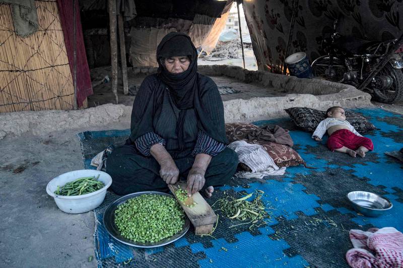 A woman prepares beans at Yunani camp, as a child sleeps nearby.
