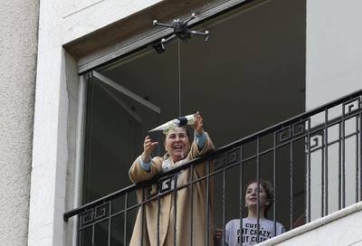 A woman standing on her balcony, reaches out to catch a rose delivered to her via a drone on Mother's day, in the Lebanese coastal city of Jounieh, north of the capital Beirut on March 21, 2020, as people remain indoors in an effort to limit the spread of the novel coronavirus. - In a quiet Lebanese town under lockdown over the novel coronavirus, a drone buzzed towards a balcony on Saturday to deliver a red rose to a mother grinning in surprise. The COVID-19 pandemic may have put a damper on Mother's Day this year, but three students have come up with a novel service to celebrate the occasion without flouting social distancing restrictions. (Photo by JOSEPH EID / AFP)