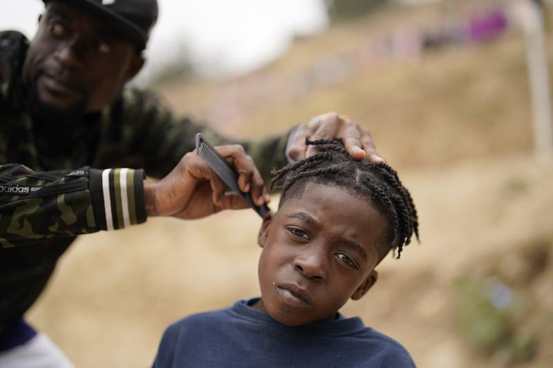 Wiggins Nordelus, of Haiti, left, cuts his son Samuel's hair outside a shelter for migrants, in Tijuana, Mexico. A federal judge in Louisiana has blocked the US government from lifting a public health order used to quickly return migrants at the southern border, including asylum-seekers. AP