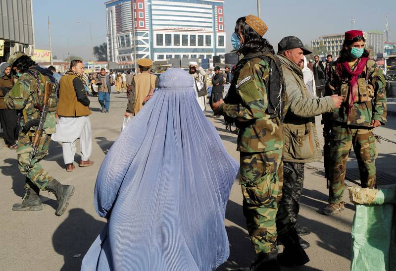 An Afghan woman wearing burqa walks past a Taliban fighter at the heavily patrolled market in Kabul on October 24, 2021. Zohra Bensemra / Reuters