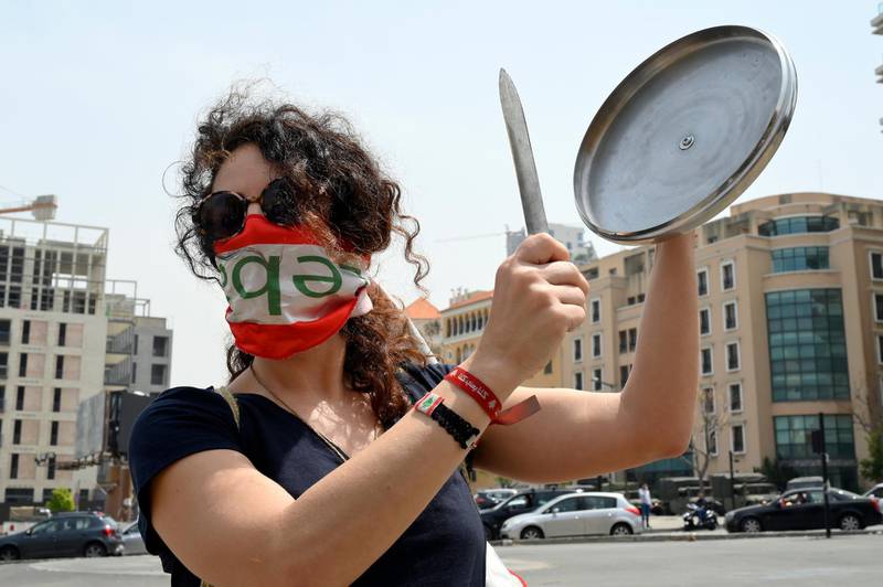 An anti-government protester bangs a knife against a lid of a pot, as she covers her face with a national flag to help curb coronavirus pandemic during a protest the economic situation in downtown Beirut.  EPA