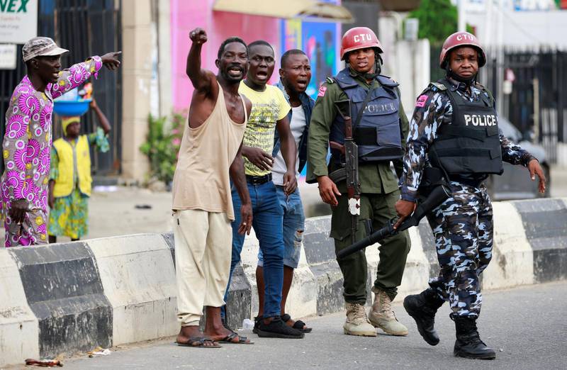 Men gesture as they stand near police officers along a street in Ikeja, as Nigeria's Lagos state remains under curfew. Reuters