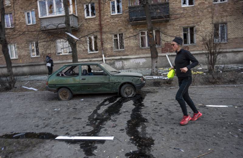 A woman exercises near a car and apartments damaged by shelling, in Kyiv. AP