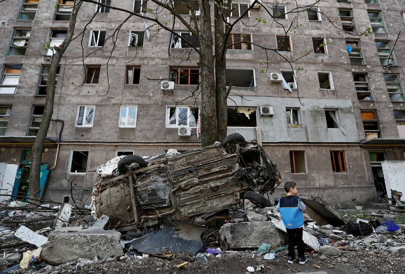 A boy stands next to a wrecked vehicle in front of an apartment damaged during the conflict in the southern port city of Mariupol. Reuters