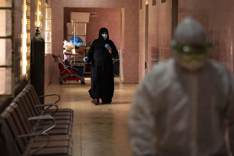 A woman wearing a surgical mask walks behind a medical staffer wearing protective gear along a hallway at Basra University Hospital, where COVID-19 coronavirus patients are treated, in the southern Iraqi city on April 1, 2020.  / AFP / Hussein FALEH

