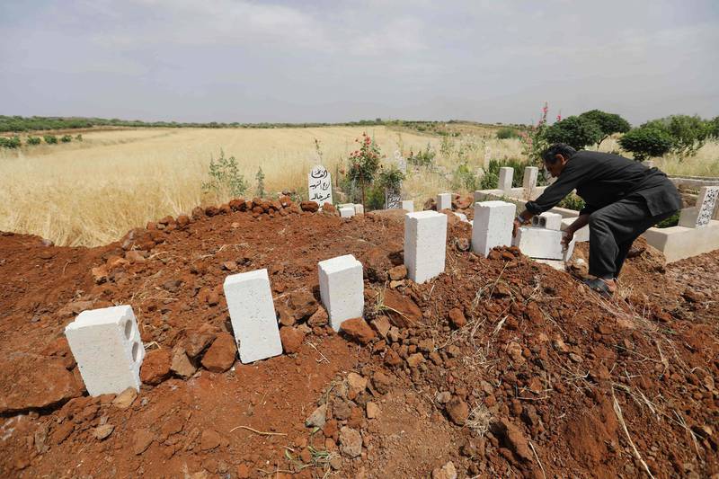 EDITORS NOTE: Graphic content / A Syrian man puts white stones over the tombs of five victims of a regime air strike on the village of Kafr Aweid in which five people, including two children, were killed  following their burial together in the country's northern Idlib province on June 5, 2019. The Idlib region of some three million people has suffered increased regime and Russian air strikes in recent weeks, with hundreds of civilians killed since late April. To keep up, civil defence workers known as the White Helmets are digging graves in advance, to ensure funerals are swift and the few who attend are not killed at the cemetery.
 / AFP / OMAR HAJ KADOUR
