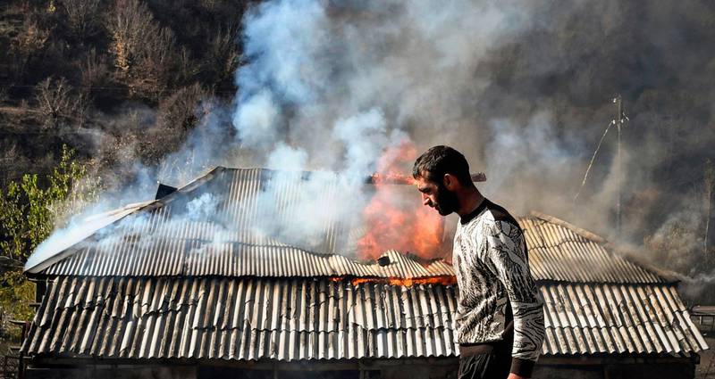 A man walks past a house burning in the village of Charektar outside the town of Kalbajar.  Villagers in Nagorno-Karabakh set their houses on fire before fleeing to Armenia.  AFP