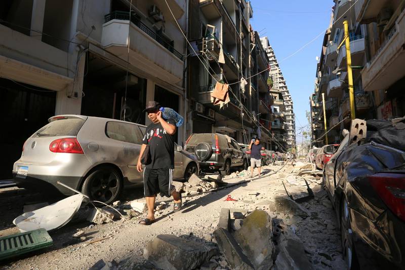 Men carrying bottles of water walk past damaged buildings and vehicles near the site of Tuesday's blast in Beirut's port area, Lebanon August 5, 2020. REUTERS/Aziz Taher
