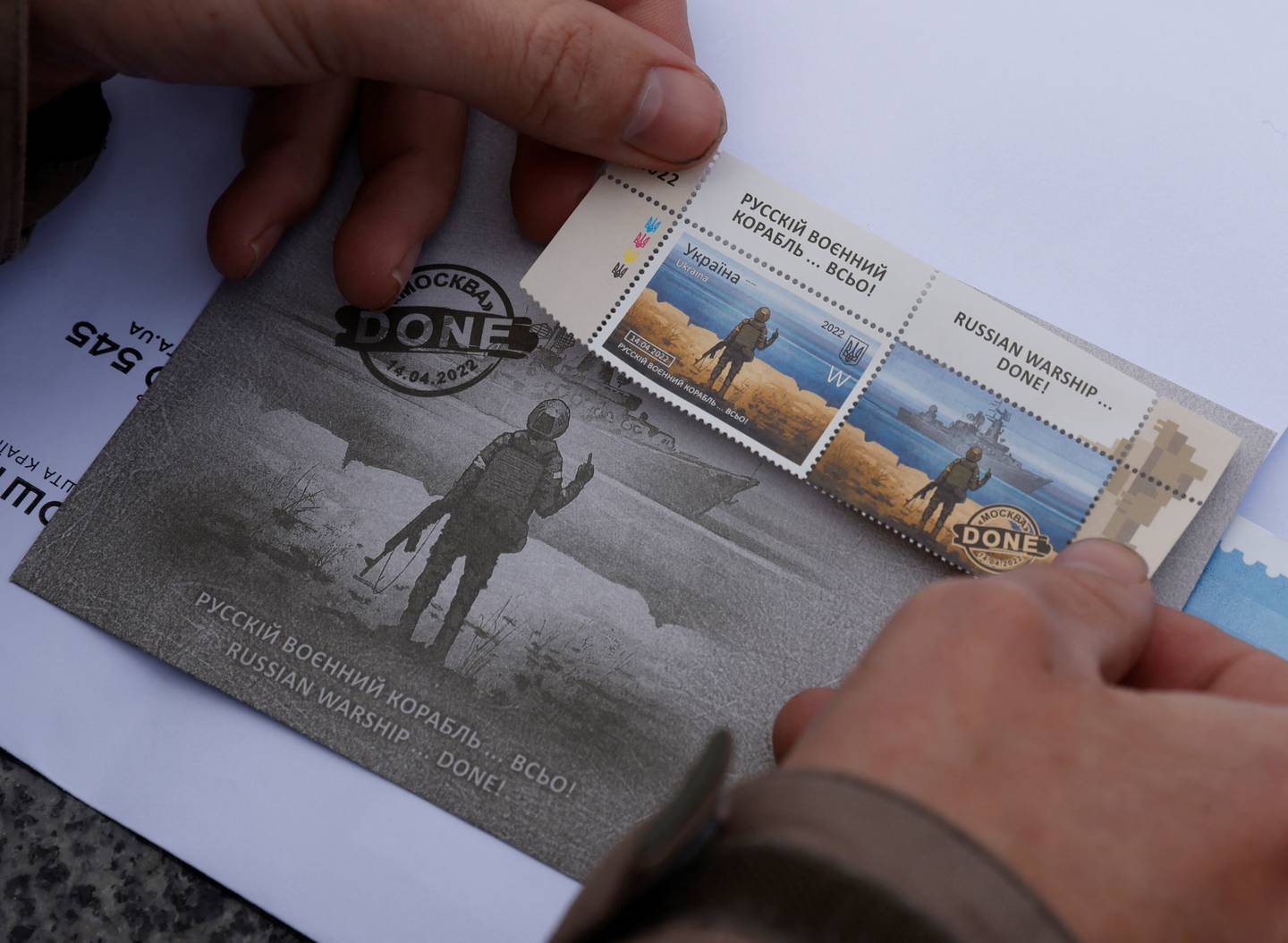 A man pastes a new series of commemorative Snake Island anti-Russian stamps on a postcard, amid the Russian invasion of Ukraine, outside the post office in Kyiv. Reuters